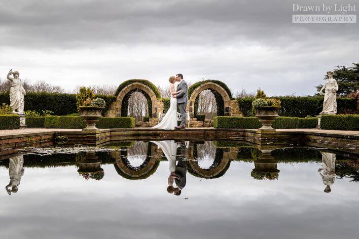 Wedding couple embracing in front of pool with reflection