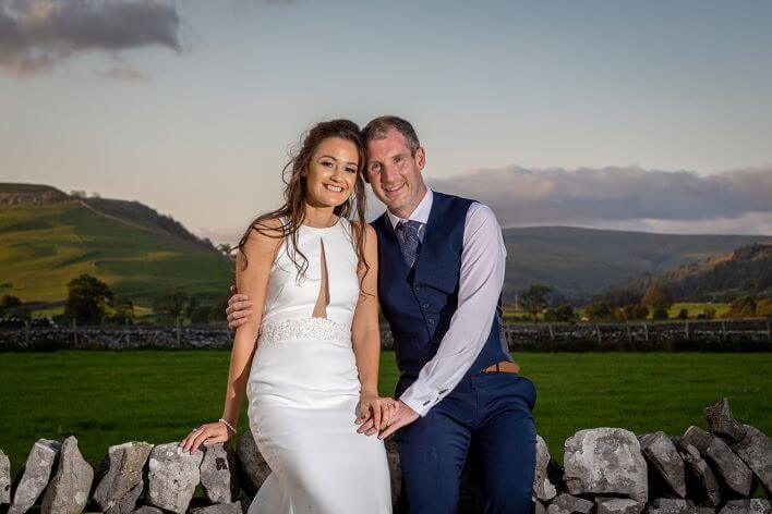 wedding couple sitting on wall with countryside in background