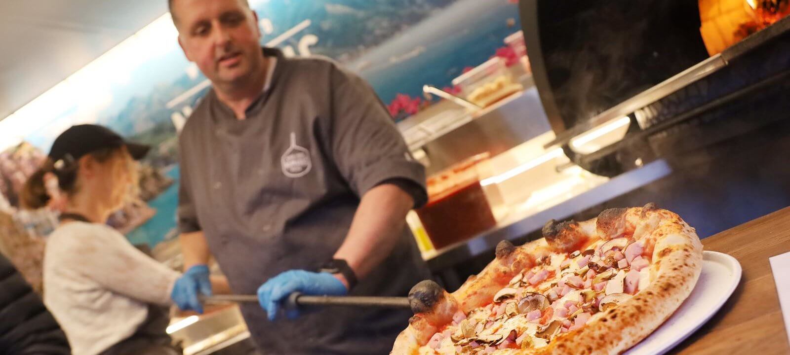 chef placing pizza on plate with pizza oven on background