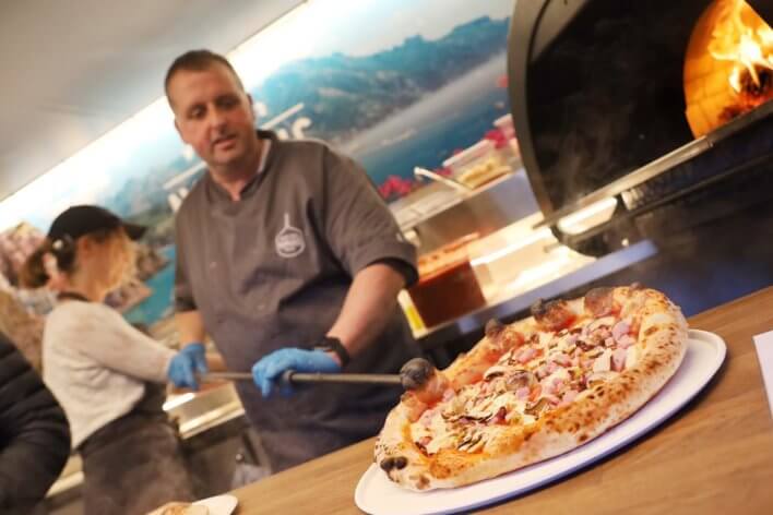 chef placing pizza on plate with pizza oven on background