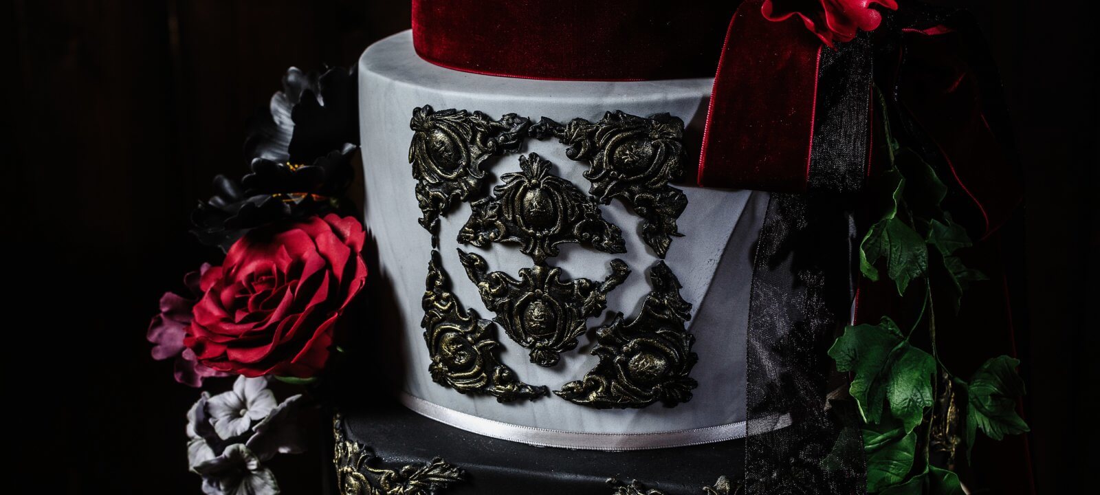 close up of wedding cake decorated with black motifs and red roses