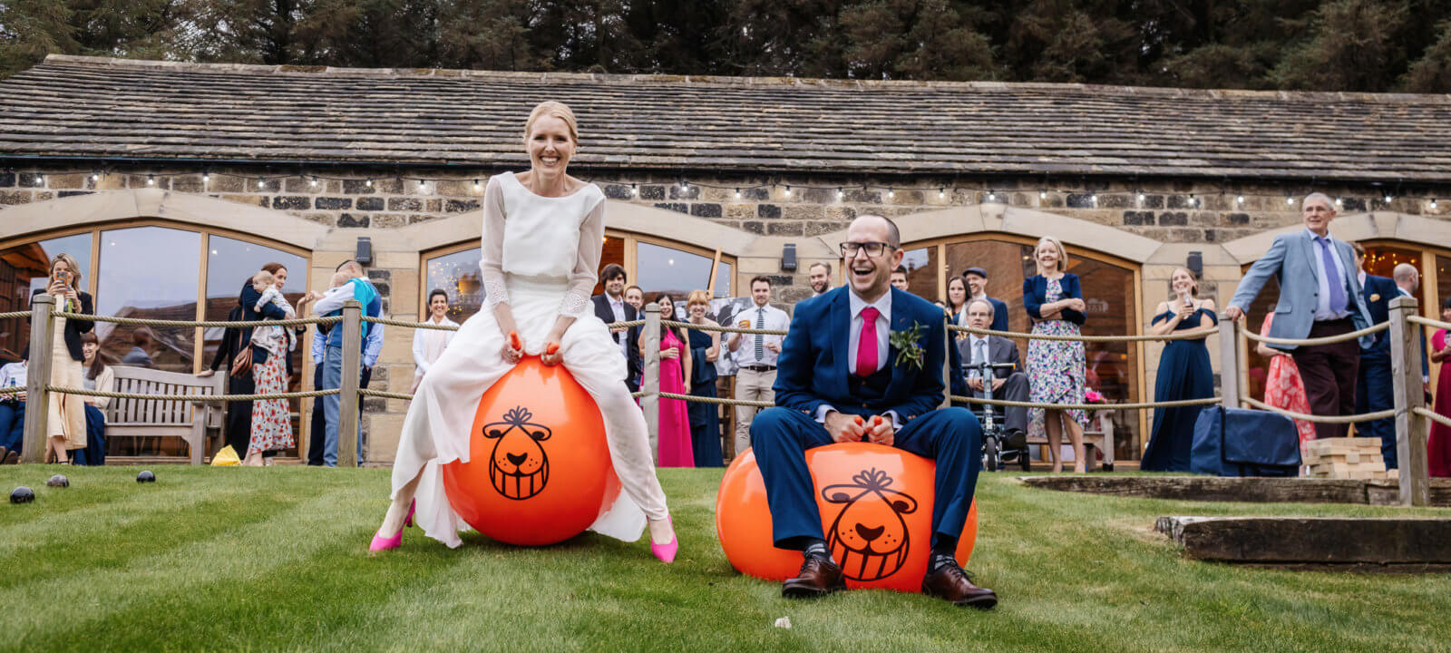 Bride and groom on space hoppers on lawn with guests looking on in background